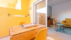 A dining area with a wooden table and chairs, a sliding glass door leading to a living room with a sofa and a cabinet. - Casa Nobre Magnifico Apartamento com Piscina (Tavira)