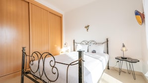 A bedroom with a bed, wooden wardrobe, and a small table with a lamp. - Casa Nobre Magnifico Apartamento com Piscina (Tavira)