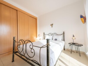 Ein Schlafzimmer mit einem Bett, einem Holzschrank und einem kleinen Tisch mit Lampe.