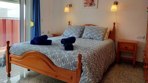 A bedroom with a wooden bed, two bedside tables, a wall-mounted artwork, and a view through a window with blinds.