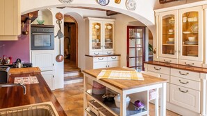 Une cuisine avec des meubles blancs, un plan de travail en bois et un îlot central. On peut y voir une cuisinière, un évier et divers ustensiles de cuisine.