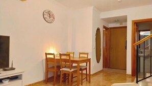 Un coin repas avec une table et des chaises en bois, une horloge au mur et un escalier menant à une autre pièce.