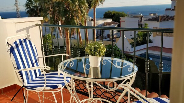 Un balcon avec deux chaises à rayures, une table en verre et une plante en pot.