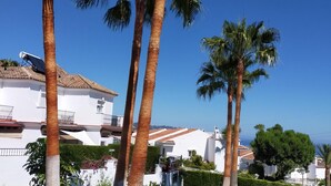 Un bâtiment blanc, surmonté d’un toit en tuiles, entouré de palmiers et s’ouvrant sur un ciel bleu azur.
