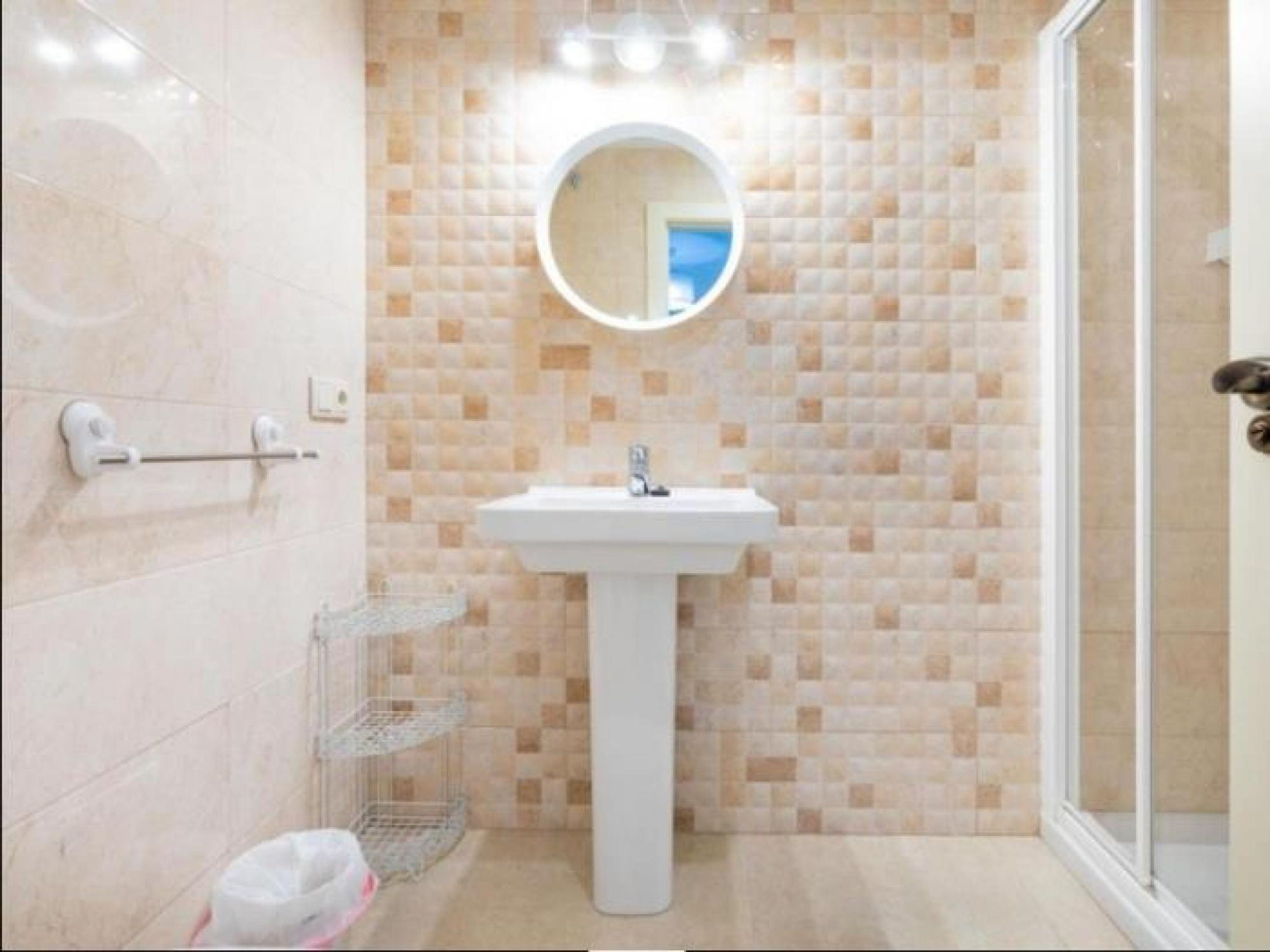 Un baño con un lavamanos blanco, un espejo y una pared de azulejos.
