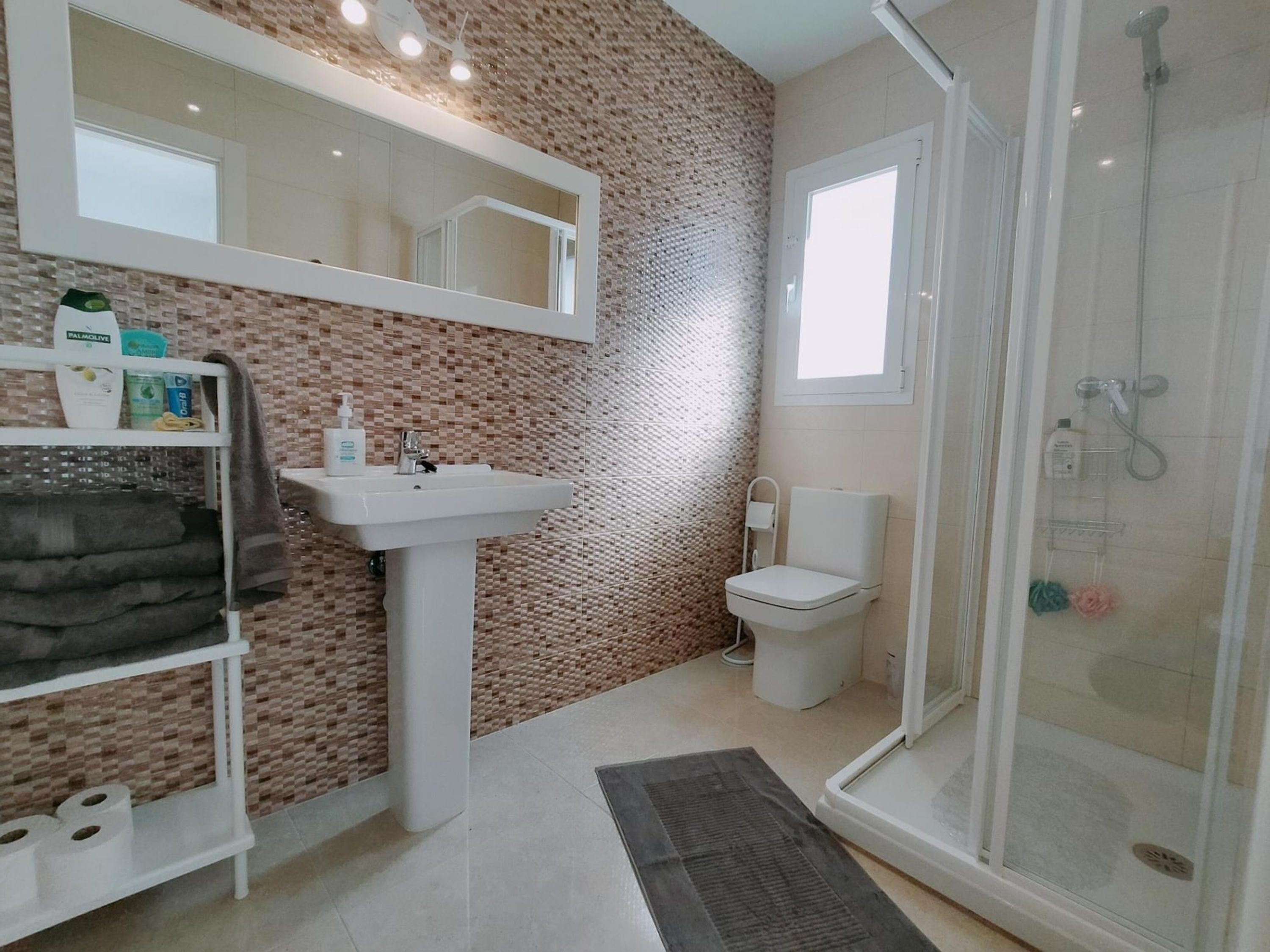 Een badkamer met een betegelde muur, een wastafel, toilet en douchegedeelte.