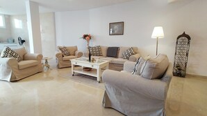 Una sala moderna con dos sofás color beige, una mesa de centro blanca y una lámpara de pie.