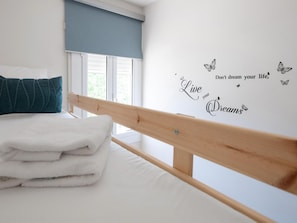 A neatly made bed with white bedding and a teal pillow, a wooden headboard, and a wall with a motivational quote and butterfly decals.