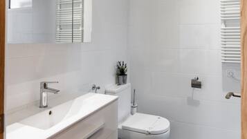 Un baño moderno con lavamanos, inodoro y tocador blancos.