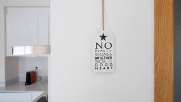 Une cuisine avec des meubles blancs, un panneau décoratif suspendu portant une citation inspirante et un cadre de porte en bois.