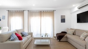 A modern living room with a beige sofa, a white coffee table, and a brown sofa. There is a flat-screen TV mounted on the wall.