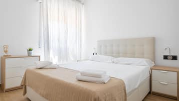 A bedroom with a large bed, a bedside table, a nightstand, a lamp, and a window with curtains.
