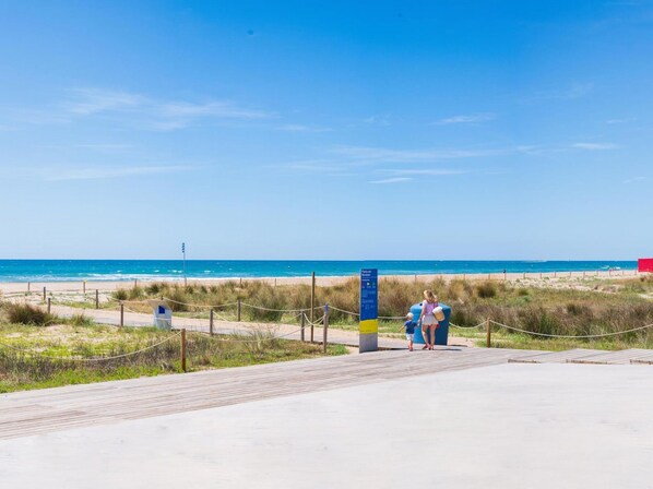 A beachside walkway leading to the ocean, with a signpost and a wooden boardwalk.