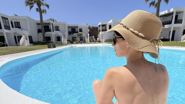 A person sitting by a swimming pool with modern buildings in the background. - Apt 27 Papagayo (Haria)
