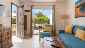 A modern living room with a blue sofa, a wooden coffee table, and a view of a garden and outdoor seating area. - Apt 27 Papagayo (Haria)