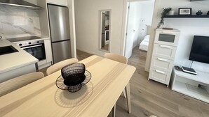 Moderni keittiö, jossa on sisäänrakennettu uuni, ruostumattomasta teräksestä valmistettu jääkaappi sekä ruokailutila, jossa on vaaleanvärinen pöytä ja tuolit.