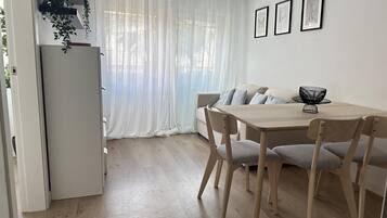 A modern, minimalist living space with a dining area, a sofa, and a refrigerator.