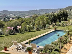 Ein rechteckiger Pool mit klarem, blauem Wasser, umgeben von einer Rasenfläche mit weißen Liegestühlen und Topfpflanzen.