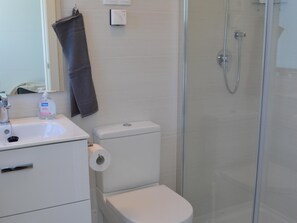 Un baño con inodoro, lavamanos, una toalla colgada en la pared y zona de ducha.
