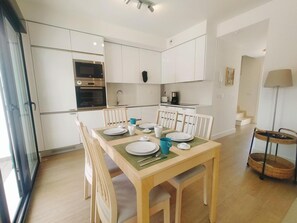 Eine moderne Küche mit weißen Schränken, einem eingebauten Backofen und einem Essbereich mit einem Holztisch, gedeckt für vier Personen.
