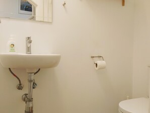 Un baño con un lavamanos blanco, un inodoro y un rollo de papel higiénico en la pared.