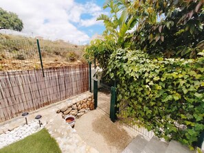 A fenced garden area with a stone wall, a small water feature, and a variety of plants including ivy and banana trees.