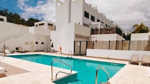 Et moderne poolområde med en klar, blå pool, liggestole og en hvid bygning med altaner.