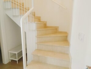 Una escalera con barandillas blancas y peldaños color beige, que sube a un piso superior.