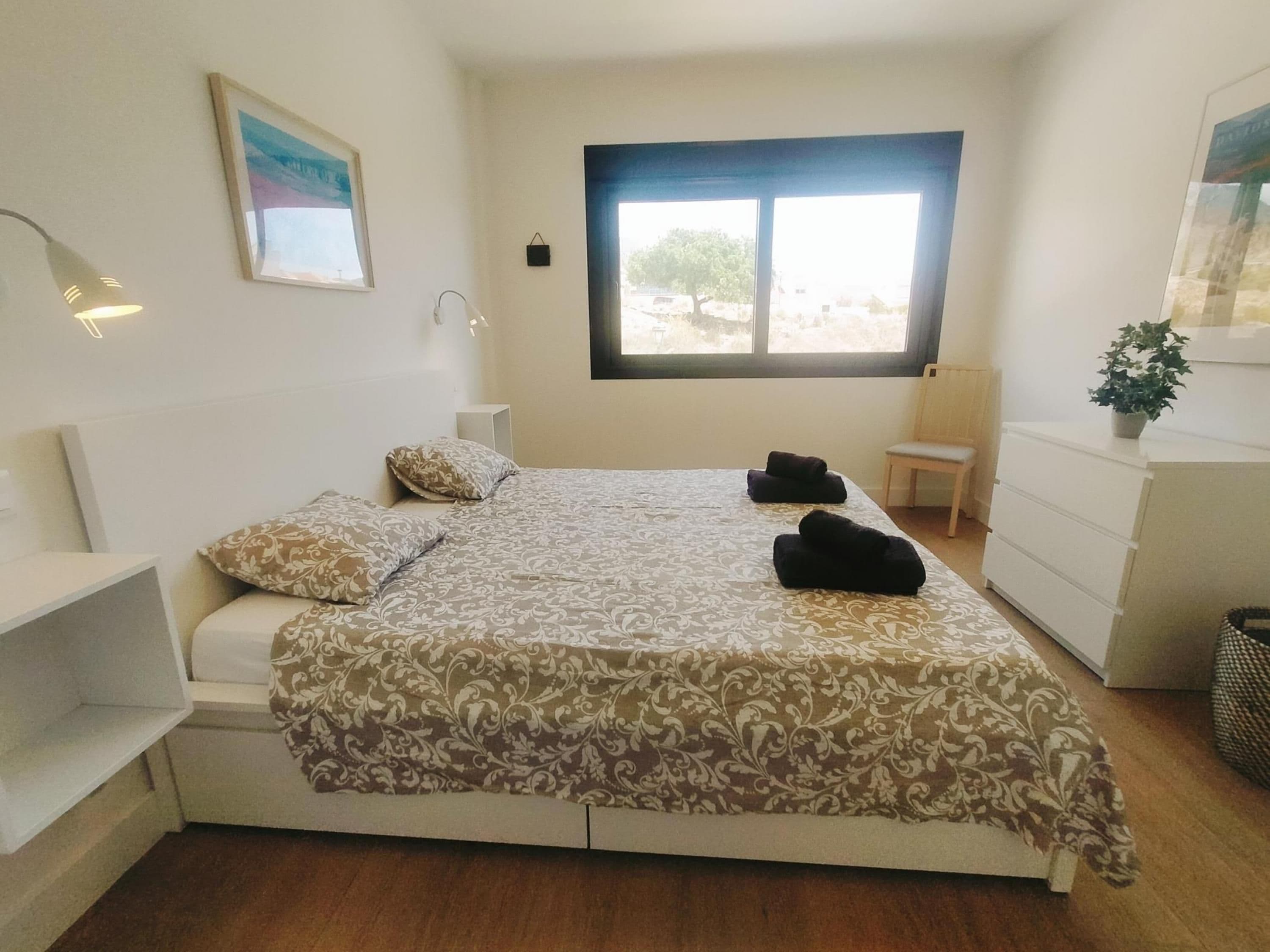 Une chambre à coucher comprenant un lit, des tables de chevet, une fenêtre, une chaise et une commode.