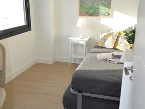 Een kleine, verzorgde slaapkamer met een bed, nachtkastje, lamp en een raam.