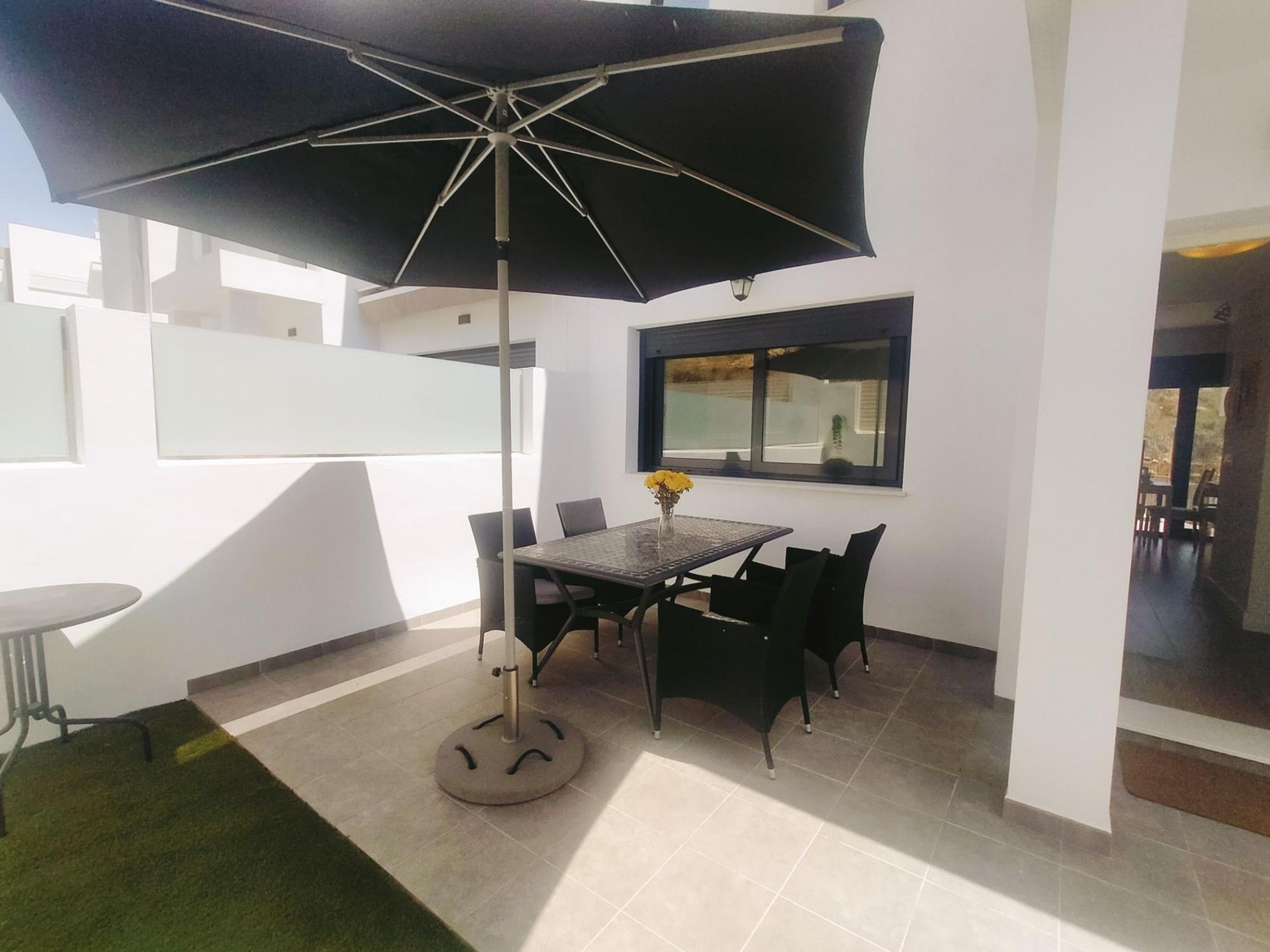 A modern outdoor dining area with a table and chairs, a large umbrella, and a view of the surrounding area.