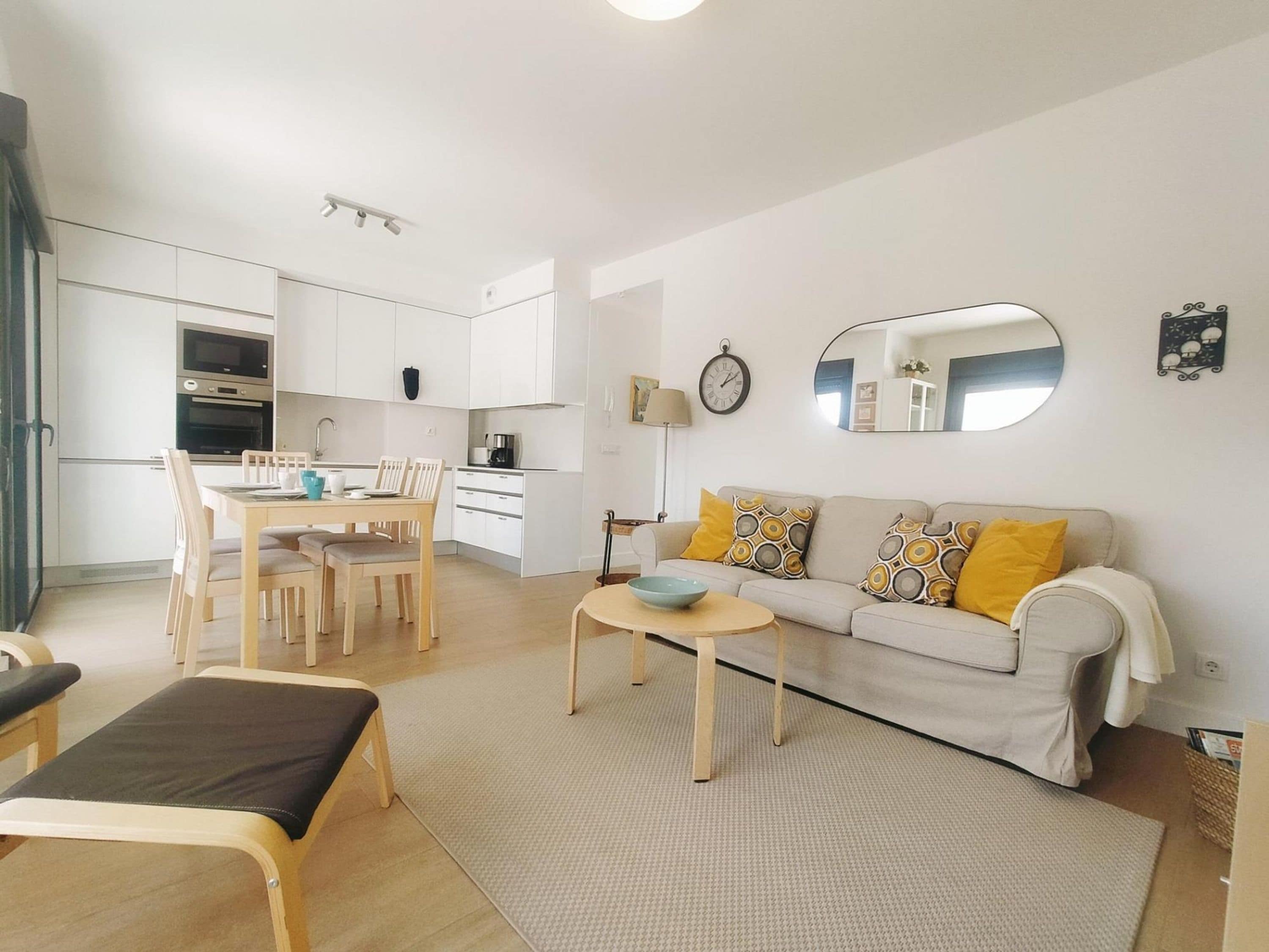 A modern apartment with a dining area, a sofa with patterned cushions, and a small table with a bowl.