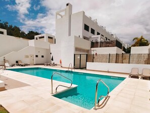 A modern pool area with a clear blue pool, sun loungers, and a white building with balconies.