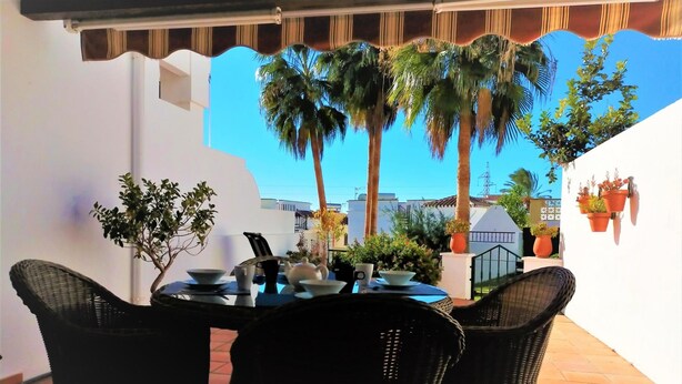 Une terrasse avec des chaises en osier, une table dressée pour le repas et des plantes en pot.