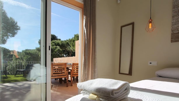 Een slaapkamer met een bed, een raam met uitzicht op een terras en een hanglamp.