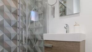 Een moderne badkamer met een douchecabine met een geometrisch patroon, een wit wastafelmeubel met een houten kast en een spiegel boven de wastafel.
