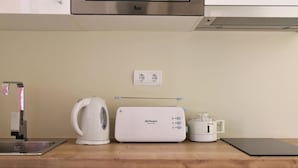 Een keuken met een roestvrijstalen afzuigkap, een waterkoker, een broodrooster en een kleine koelkast.