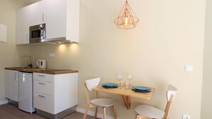 Een compacte keuken met een magnetron, waterkoker en een eethoek met een tafel en stoelen.