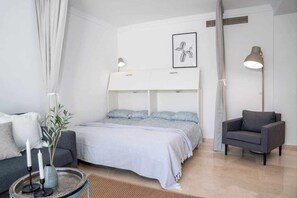 A modern bedroom with a bed, bedside tables, a chair, and a lamp. - Aloha Pueblo Beautiful Apartment With Roof Terrace (Marbella)