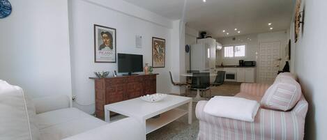 Una sala de estar con sofá, televisor, mesa de centro y comedor con sillas y mesa.