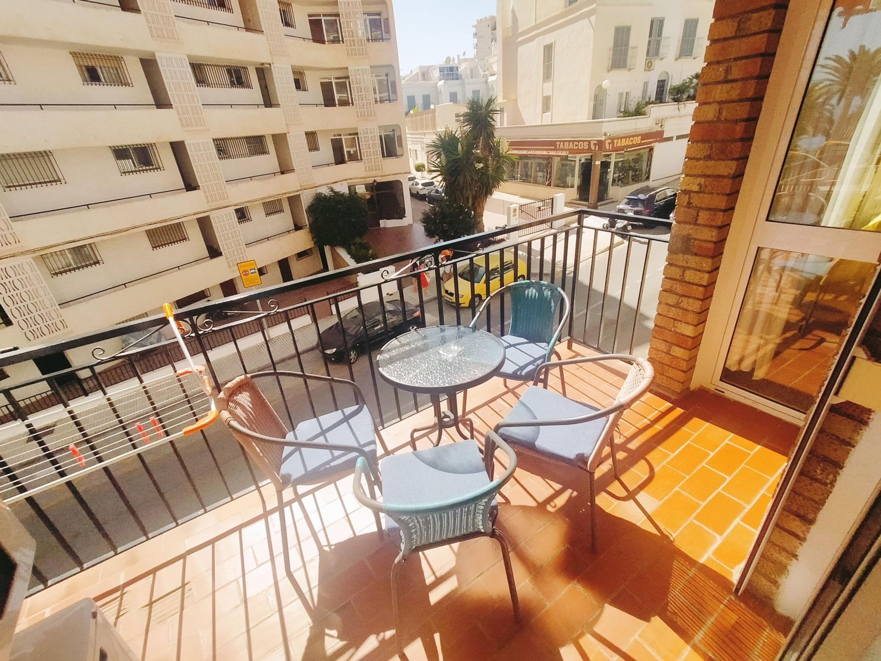 Un balcone con tavolo e sedie, vista sulla strada e un palazzo con balconi sullo sfondo.