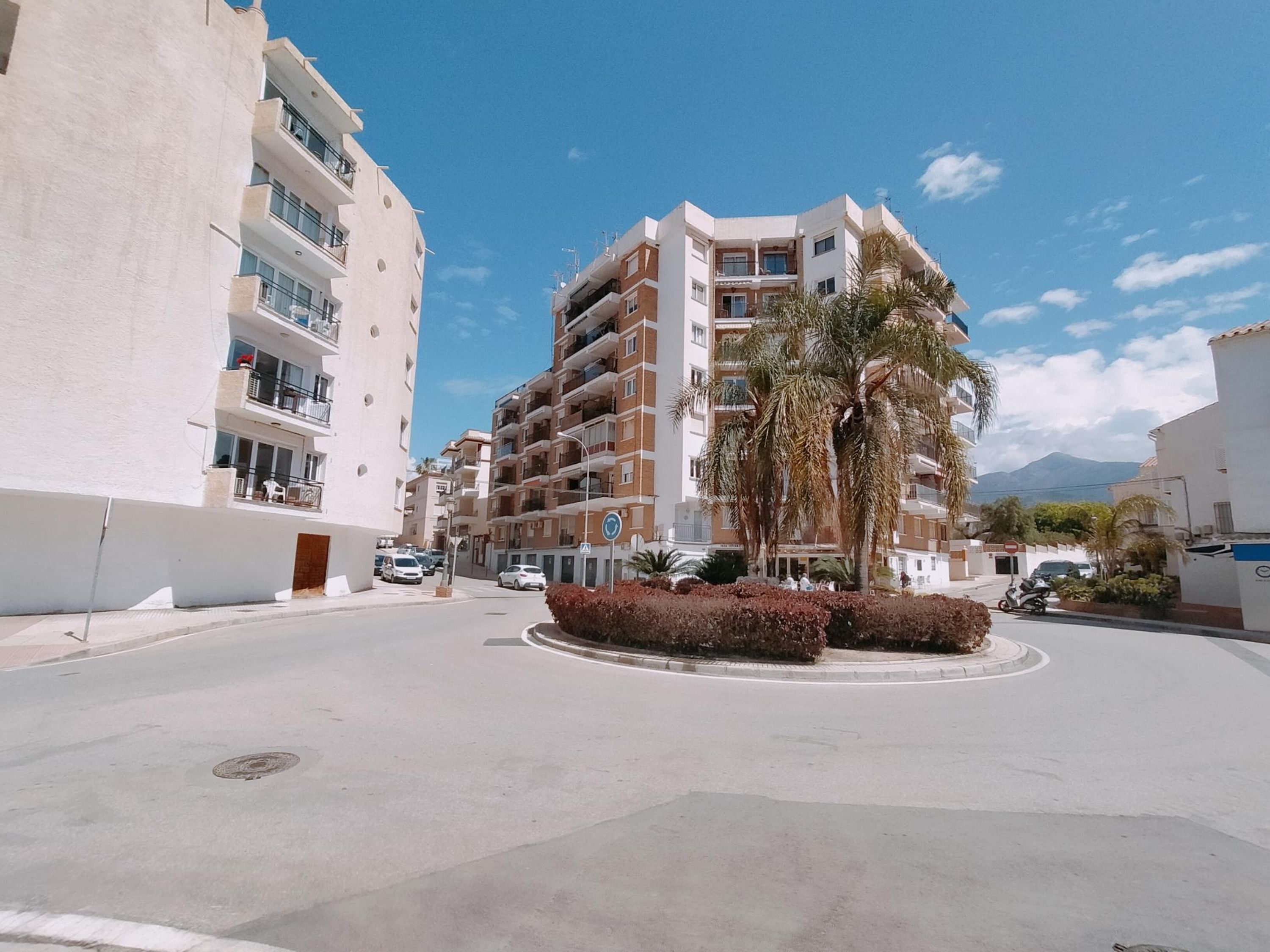 Un edificio residencial de varios pisos con balcones, una glorieta y palmeras.