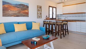 A living room with a blue sofa, wooden coffee table, and a painting of a desert landscape. - Apt 26 Timanfaya (Haria)
