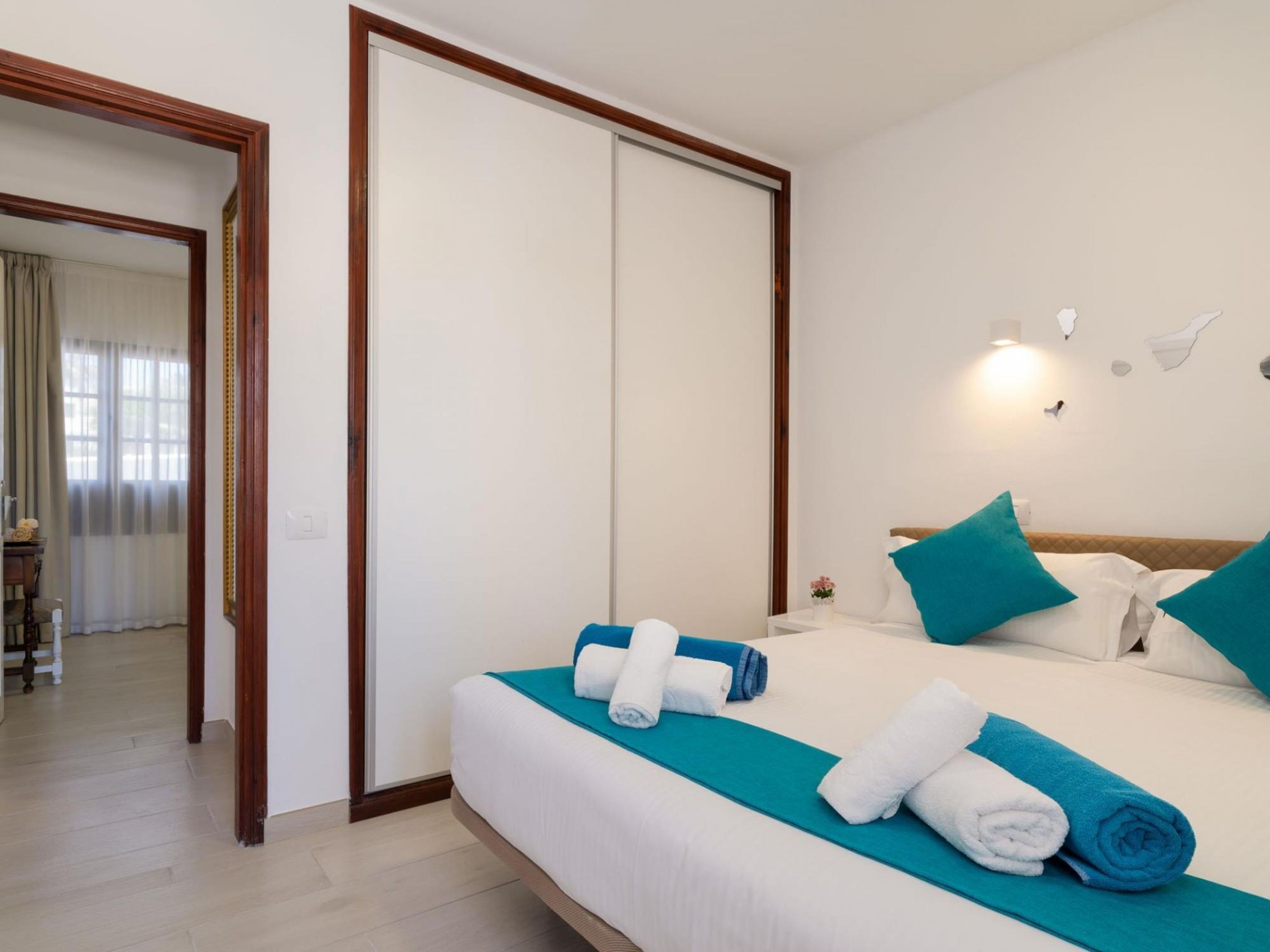 A hotel room with a bed, a nightstand, a mirror, and a door leading to another room.