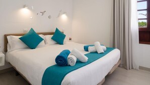 A double bed with teal and white bedding, a small bedside table with a lamp, and a window with curtains. - Apt 32 Las Malvas (Haria)