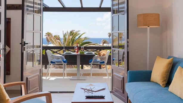 Un balcon ouvert avec une table dressée pour deux personnes, un canapé et une lampe.