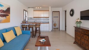 Un salon moderne avec un canapé bleu, une table basse en bois et une cuisine en arrière-plan.