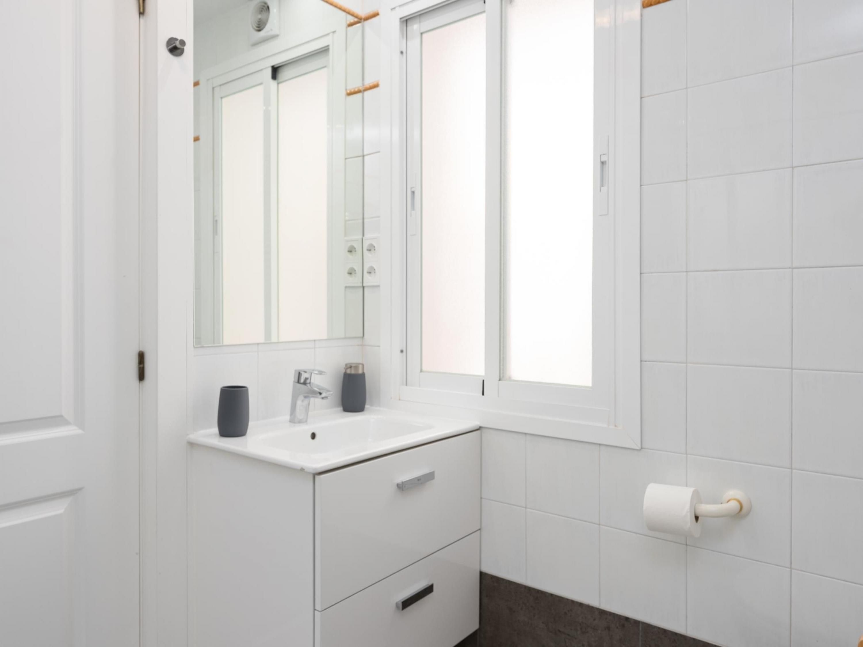 A modern bathroom with a white vanity, a mirror, a toilet, and a window.