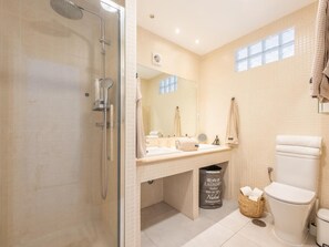 A bathroom with a glass-enclosed shower, a sink with a mirror, a toilet, and a laundry basket.