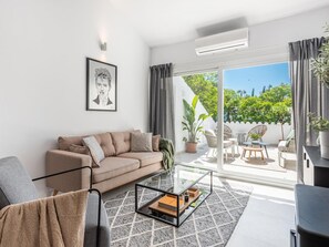 A modern living room with a sofa, a glass coffee table, and a view of a balcony with outdoor furniture and plants. - Agrupadas Beautiful Duplex With Amazing Location (Marbella)